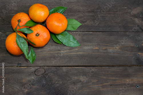 Fresh orange mandarins with green leaves on a dark wooden table. The concept of a healthy diet and vegetarianism. Top view.