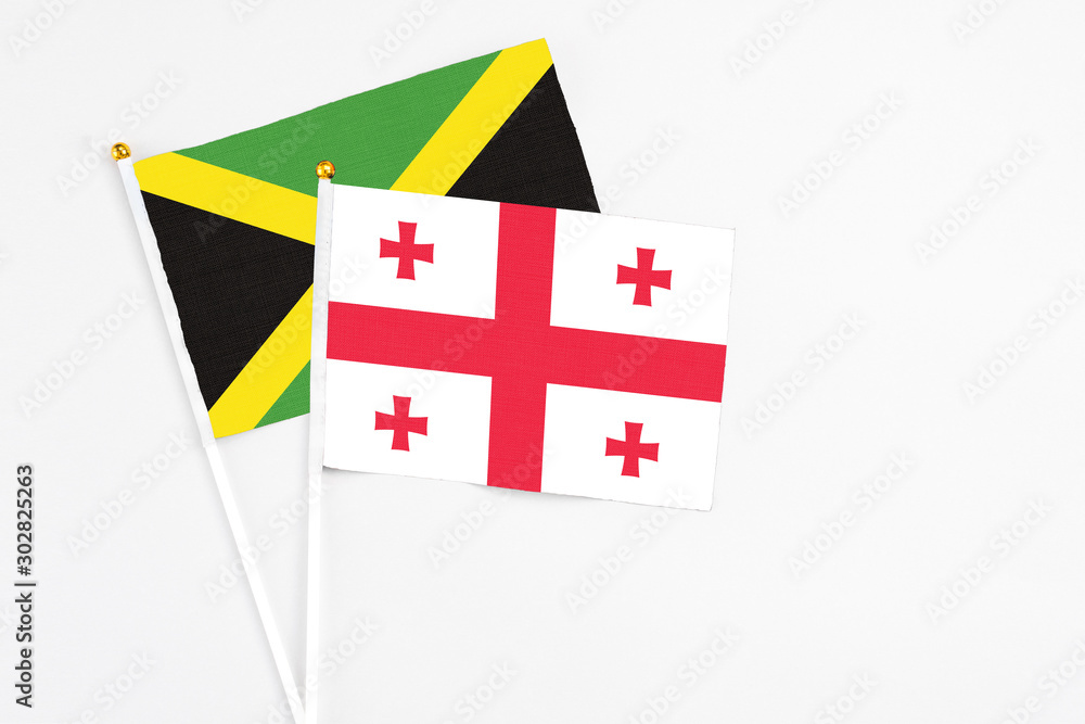 Georgia and Jamaica stick flags on white background. High quality fabric, miniature national flag. Peaceful global concept.White floor for copy space.