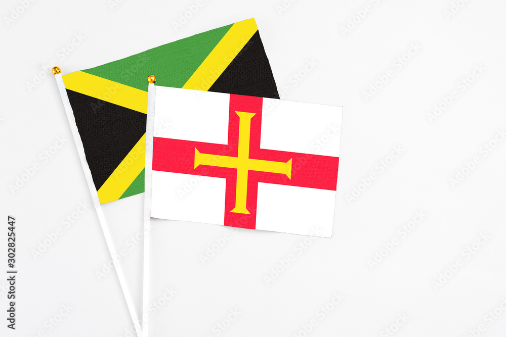 Guernsey and Jamaica stick flags on white background. High quality fabric, miniature national flag. Peaceful global concept.White floor for copy space.