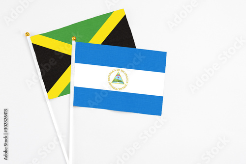 Nicaragua and Jamaica stick flags on white background. High quality fabric, miniature national flag. Peaceful global concept.White floor for copy space.