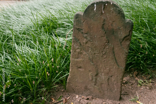 Unmarked old graveyard tombstone surrounded by dirt and tall green grass