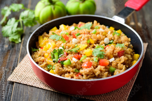 Fried rice with vegetables in cooking pan on wooden table, Asian food
