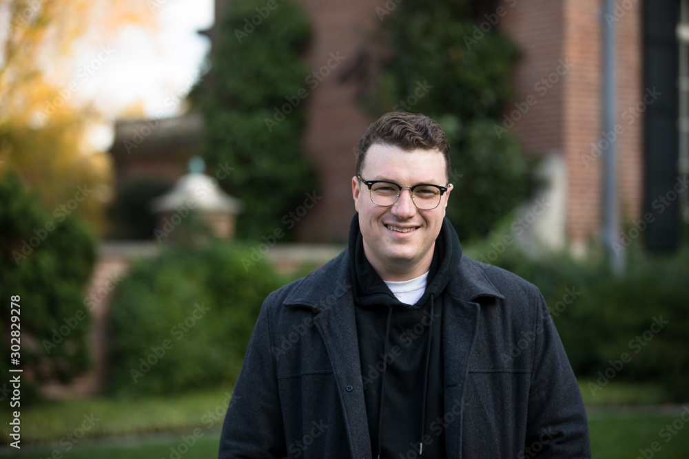 A caucasian male wearing a black hoodie sweater and glasses poses in a garden while surrounded by fall foliage on a cold afternoon. A caucasian male wearing a black hoodie sweater and glasses poses in a garden while surrounded by fall foliage on a cold afternoon.