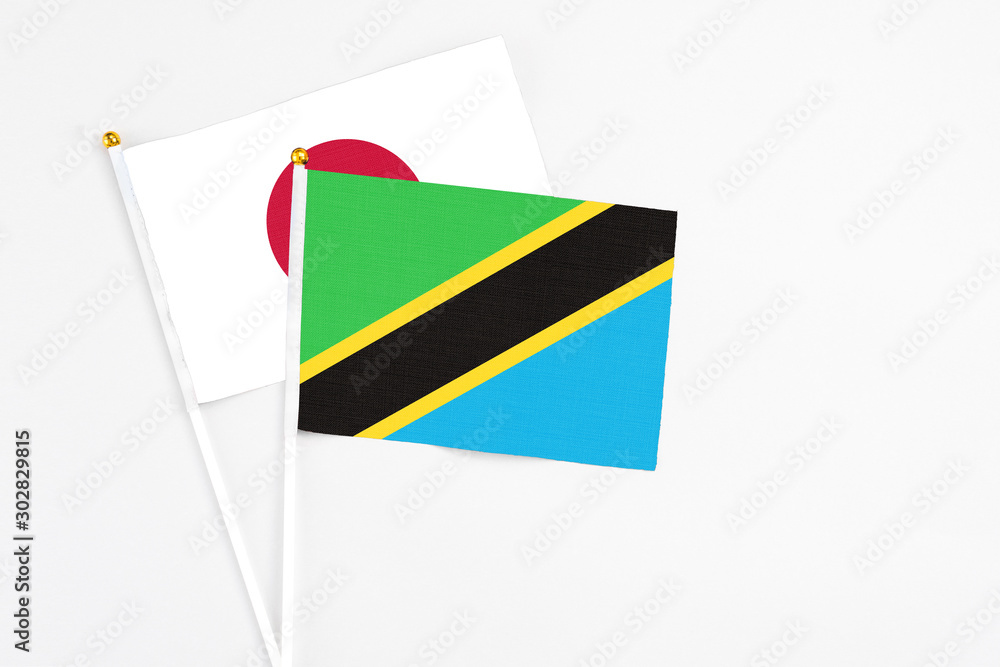Fototapeta premium Tanzania and Japan stick flags on white background. High quality fabric, miniature national flag. Peaceful global concept.White floor for copy space.