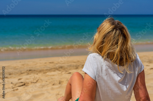 A woman with blond hair sits on the beach and has the view of the sea
