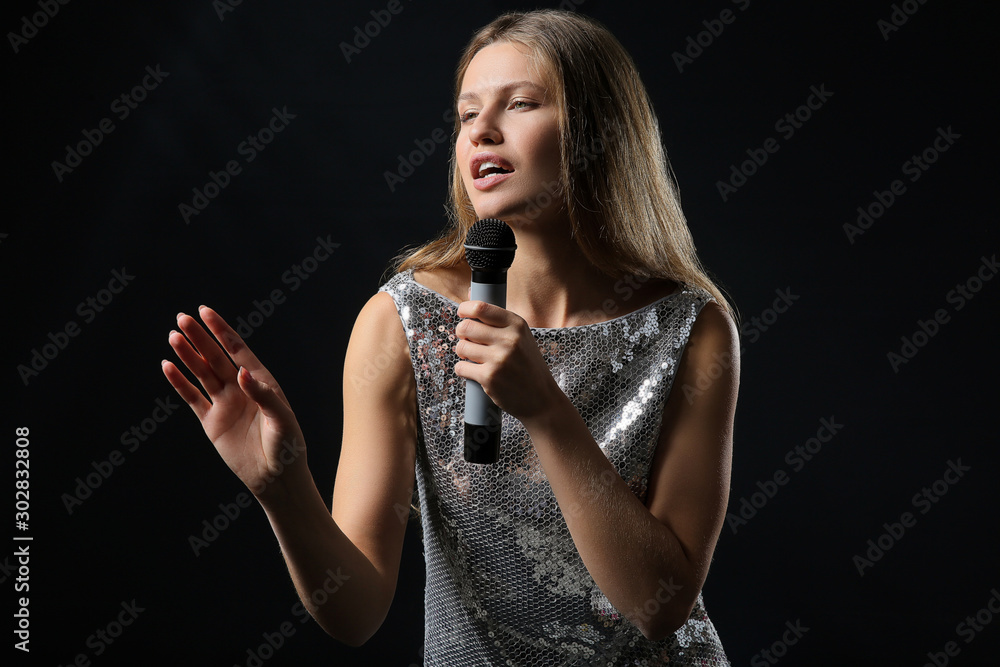 Beautiful young female singer with microphone on dark background