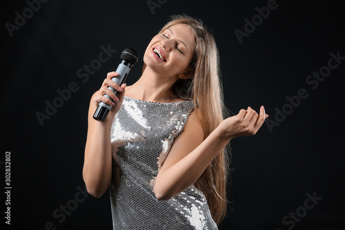 Beautiful young female singer with microphone on dark background © Pixel-Shot