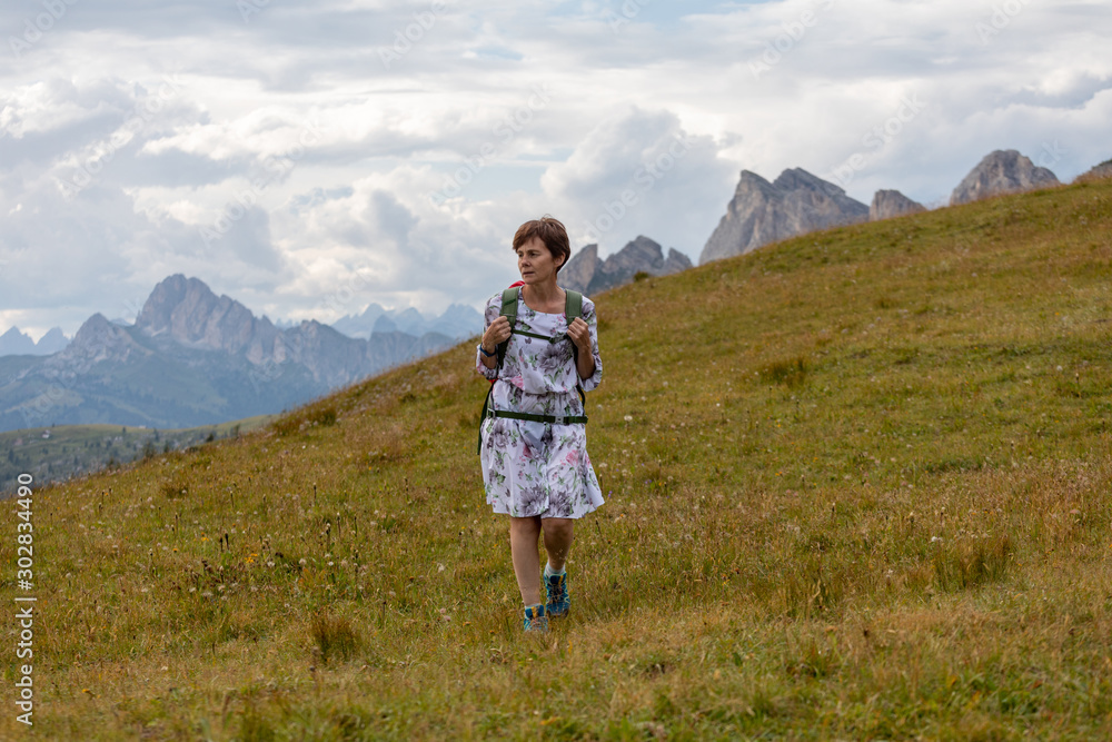 Girl in a dress and with a backpack on a background of mountains. Mountain valley of the Alps, Dolomites. Summer sunny day