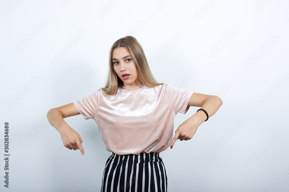 Portrait of excited young woman in casual shirt pointing index fingers down, looking camera isolated on white wall background in studio. People lifestyle concept. Portrait of excited young woman in casual shirt pointing index fingers down, looking camera isolated on white wall background in studio. People lifestyle concept.