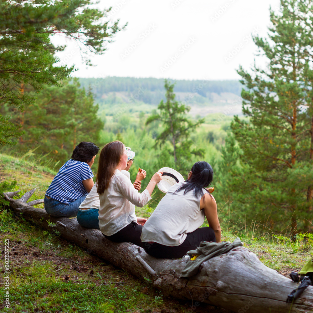 Four girls Yakut friends sitting on a log and communicate against the background of the wild North of the taiga and streams.
