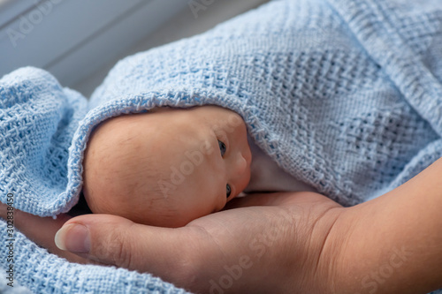 premature newborn baby wrapped in blue blanket with mothers  arm and hand represented by a reborn doll; background for copy space and text overlay photo