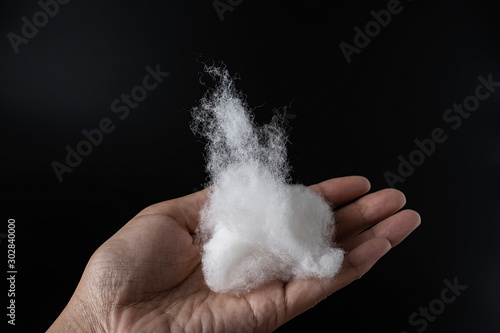 Hand holding a long pile of cotton on a black background