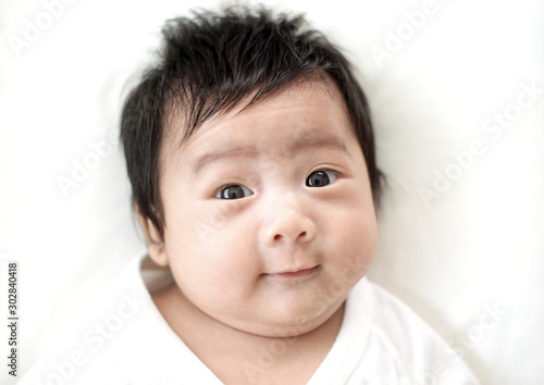Cute adorable asian newborn looking at camera and smiling on white bed : Closeup photo