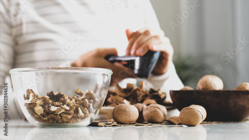 Young woman is cracking a walnuts at home. She collects a nuts in glass while sits at the table in domestic room, close-up.