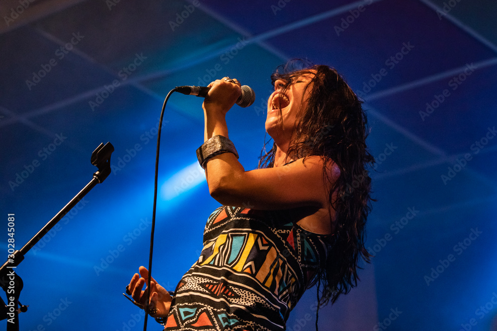 A female musician is viewed from a low angle as she sings, with open mouth in microphone during a performance on stage - obrazy, fototapety, plakaty 