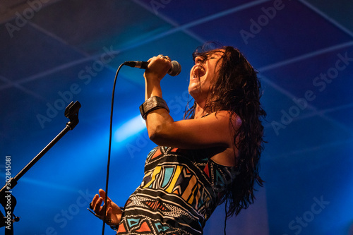 A female musician is viewed from a low angle as she sings, with open mouth in microphone during a performance on stage