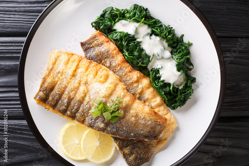 Canvas Print Tasty grilled sea bass fillet with spinach and lemon close-up on a plate