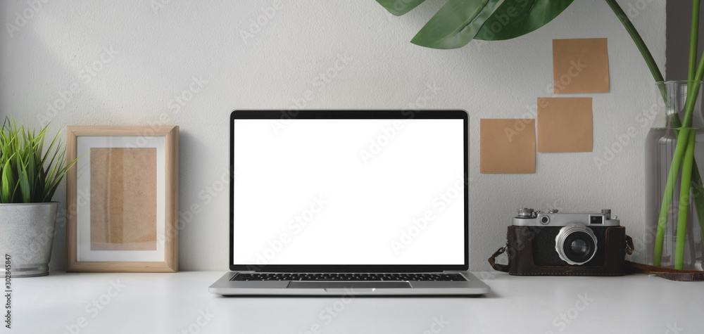 Obraz premium Modern office room with blank screen laptop computer and camera with office supplies