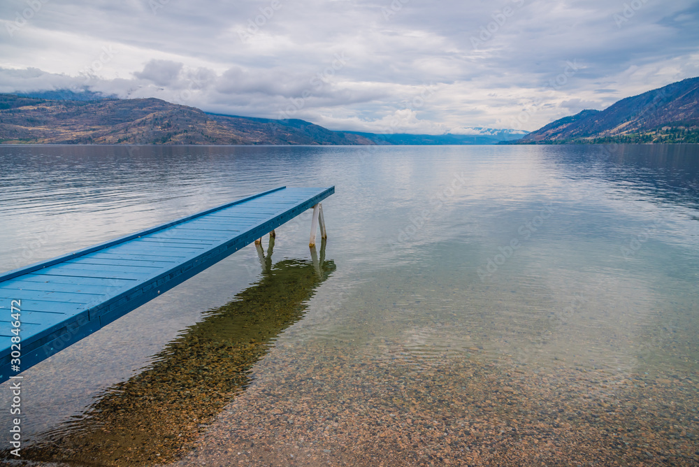 Naklejka premium Blue painted dock extending over calm lake with view of overcast sky and mountains