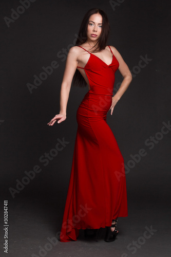 portrait of a young dark-haired girl on a dark background, dancing in a red long dress