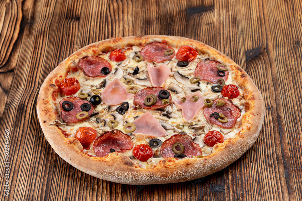 Hot meat pizza with pepperoni, salami, ham, melted cheese and olives on wooden table Hot meat pizza with pepperoni, salami, ham, melted cheese and olives on wooden table