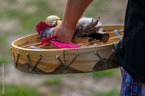 A close-up view of a person's hand holding a traditional native drum, drumsticks and pieces of wood, during a music celebration in the park photo