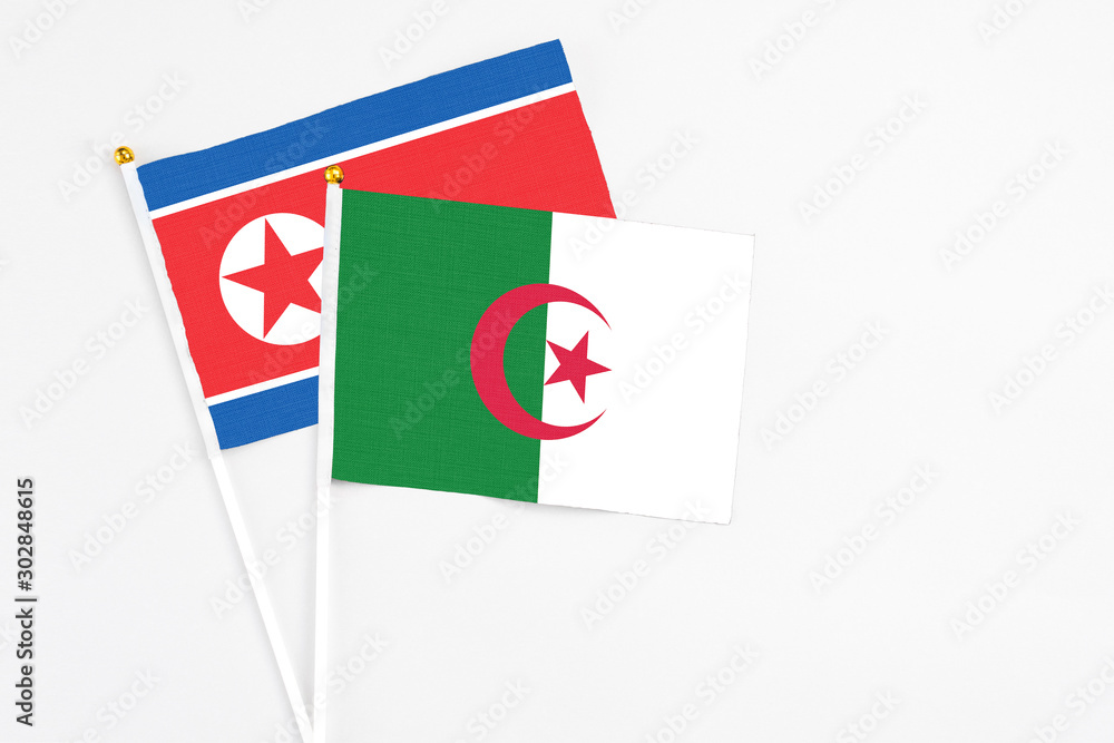 Algeria and North Korea stick flags on white background. High quality fabric, miniature national flag. Peaceful global concept.White floor for copy space. Algeria and North Korea stick flags on white background. High quality fabric, miniature national flag. Peaceful global concept.White floor for copy space.