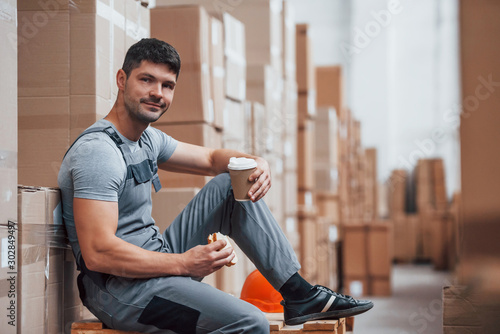 Storage worker sits and have a break. Eats sandwitch and drinks coffee