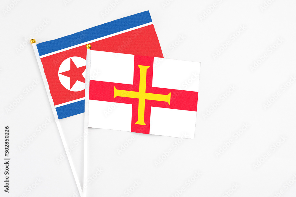 Guernsey and North Korea stick flags on white background. High quality fabric, miniature national flag. Peaceful global concept.White floor for copy space.