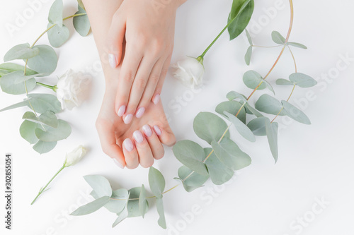 Stylish plain female hand manicure gel polish on white flower background eucalyptus, top view. Concept natural organic skin care