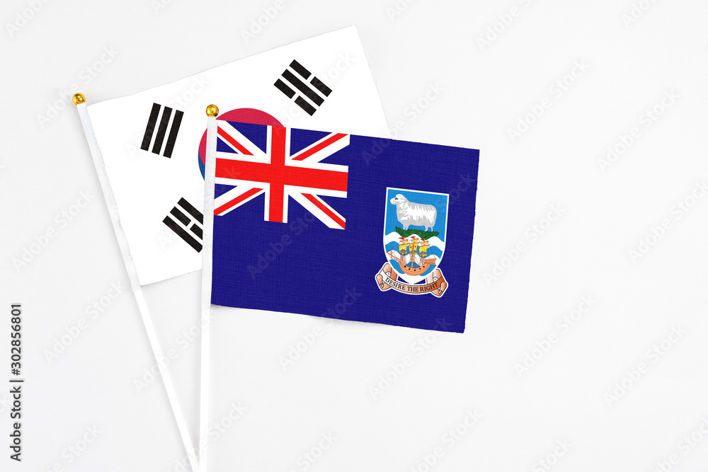 Fototapeta premium Falkland Islands and South Korea stick flags on white background. High quality fabric, miniature national flag. Peaceful global concept.White floor for copy space.