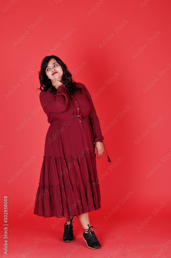 Attractive south asian woman in deep red gown dress posed at studio on pink background. Attractive south asian woman in deep red gown dress posed at studio on pink background.