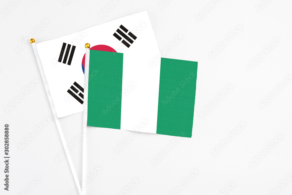 Nigeria and South Korea stick flags on white background. High quality fabric, miniature national flag. Peaceful global concept.White floor for copy space. Nigeria and South Korea stick flags on white background. High quality fabric, miniature national flag. Peaceful global concept.White floor for copy space.