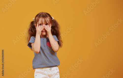 Cute little girl in casual clothes have fun in the studio against yellow background