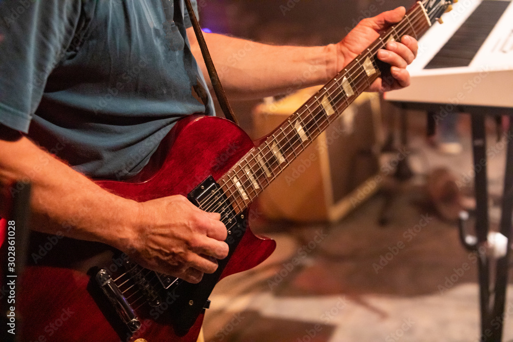 close up and selective focus on man's red electric guitar as he playing, with a blurry studio ground background