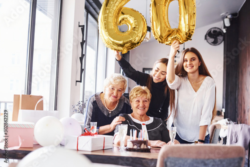 Balloons with number 60. Senior woman with family and friends celebrating a birthday indoors