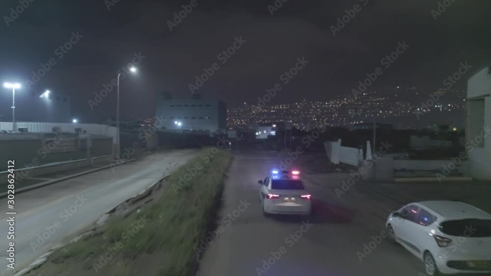 Night aerial footage of a police car driving down a dark urban area ...