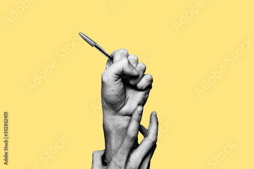 Concept of freedom of speech and information, stop censorship. Hand holding an open pen. It is dragged down by another hand. Black and white subject with a yellow background