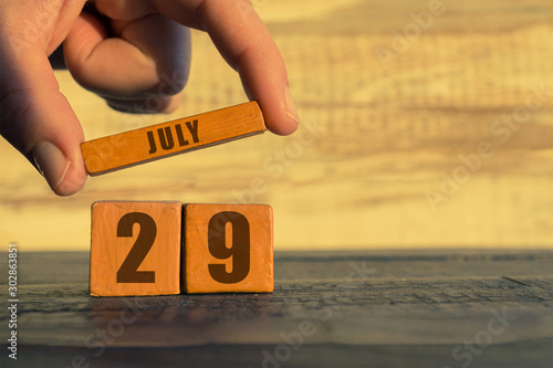 july 29th. Day 29 of month,calendar on a wooden cube. a woman's hand puts the name of the month on the number of the month on a wooden background summer, day of the year concept photo