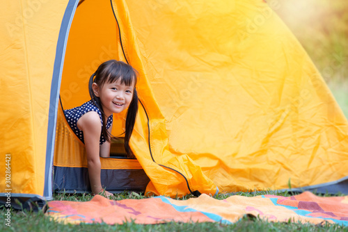 Little Asian girl smile and looking at camera playing with her tent on campsite  happy girl sitting inside yellow tent at park