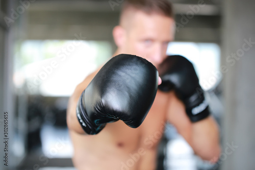 Sportsman muay thai boxer fighting in gloves in boxing cage against fitness gym. Copy Space. © FotoArtist