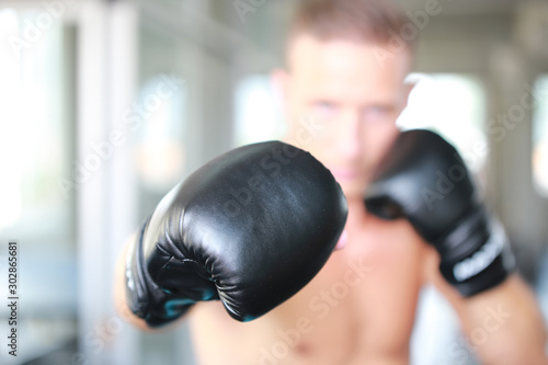 Sportsman muay thai boxer fighting in gloves in boxing cage against fitness gym. Copy Space. © FotoArtist
