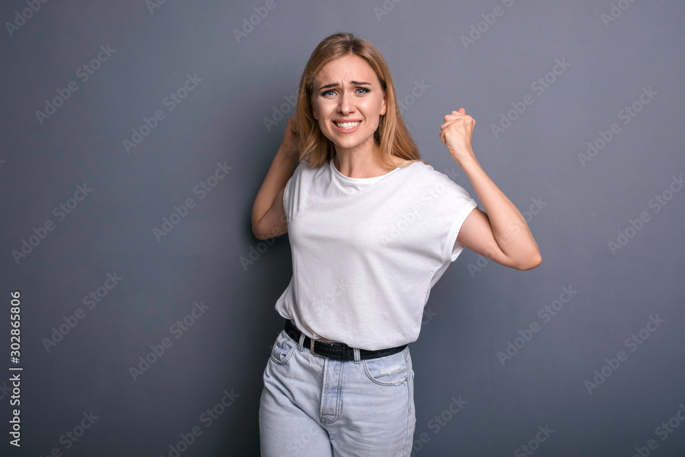 Caucasian woman in neutral casual outfit standing on a neutral grey background. Portrait with emotions: angry, pain, sickness and despair Caucasian woman in neutral casual outfit standing on a neutral grey background. Portrait with emotions: angry, pain, sickness and despair