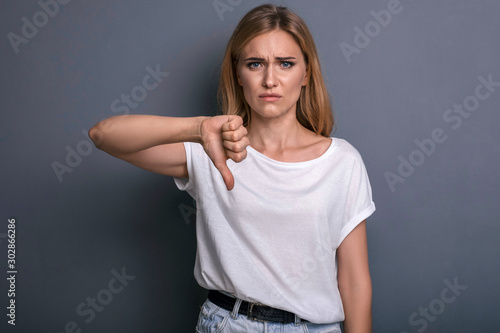 Caucasian woman in neutral casual outfit standing on a neutral grey background. Portrait with emotions: angry, pain, sickness and despair