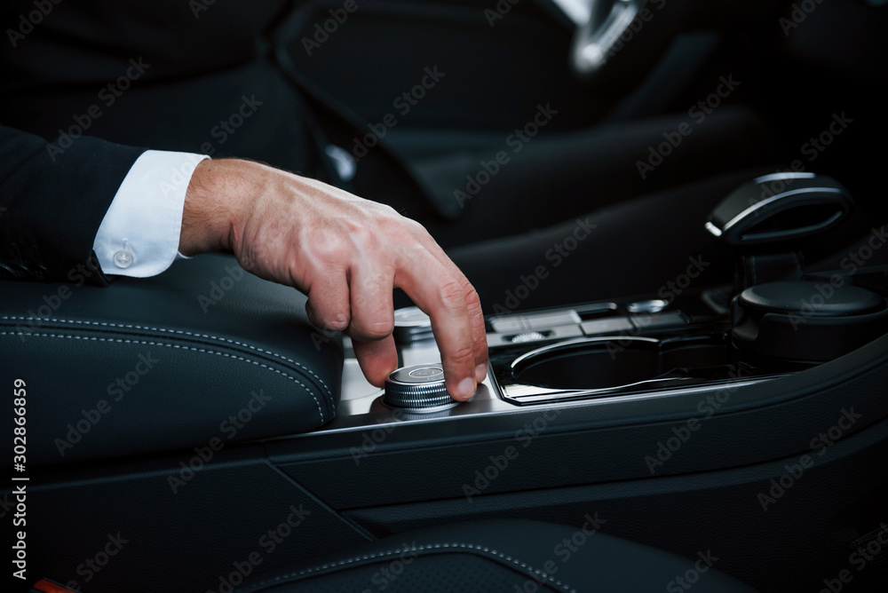 Close up view of hand of man in black suit inside modern automobile