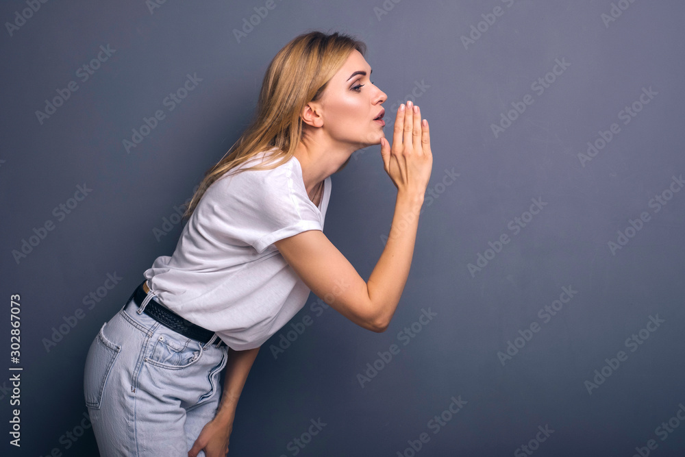 Caucasian woman in neutral casual outfit standing on a neutral grey background. Portrait with emotions: happiness, amazement, joy and satisfaction while whispering secrets Caucasian woman in neutral casual outfit standing on a neutral grey background. Portrait with emotions: happiness, amazement, joy and satisfaction while whispering secrets