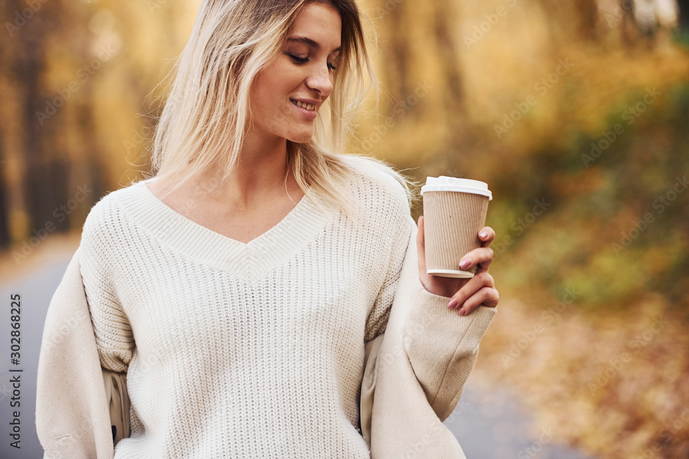 Holds cup of drink. Portrait of young brunette that is in autumn forest at daytime Holds cup of drink. Portrait of young brunette that is in autumn forest at daytime