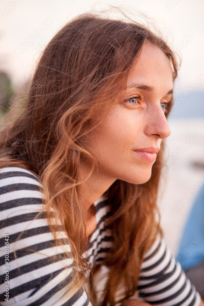 Portrait of a beautiful red-haired girl in T-shirt near the sea at the sunset. Pensive and happy girl. Relaxing near ocean. pretty girl Portrait of a beautiful red-haired girl in T-shirt near the sea at the sunset. Pensive and happy girl. Relaxing near ocean. pretty girl