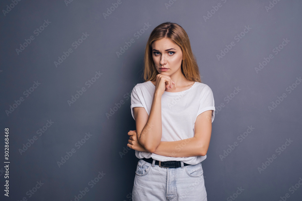 Caucasian woman in neutral casual outfit standing on a neutral grey background. Portrait with emotions: angry, pain, sickness and despair Caucasian woman in neutral casual outfit standing on a neutral grey background. Portrait with emotions: angry, pain, sickness and despair