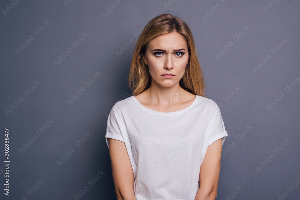 Caucasian woman in neutral casual outfit standing on a neutral grey background. Portrait with emotions: angry, pain, sickness and despair Caucasian woman in neutral casual outfit standing on a neutral grey background. Portrait with emotions: angry, pain, sickness and despair